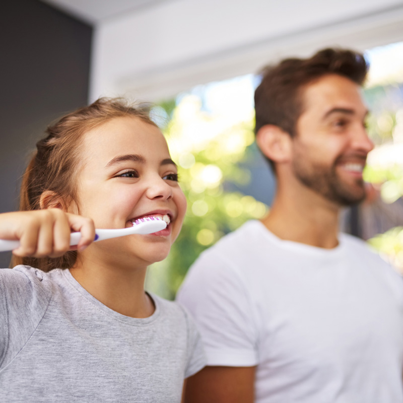 little kid brushing teeth along side father