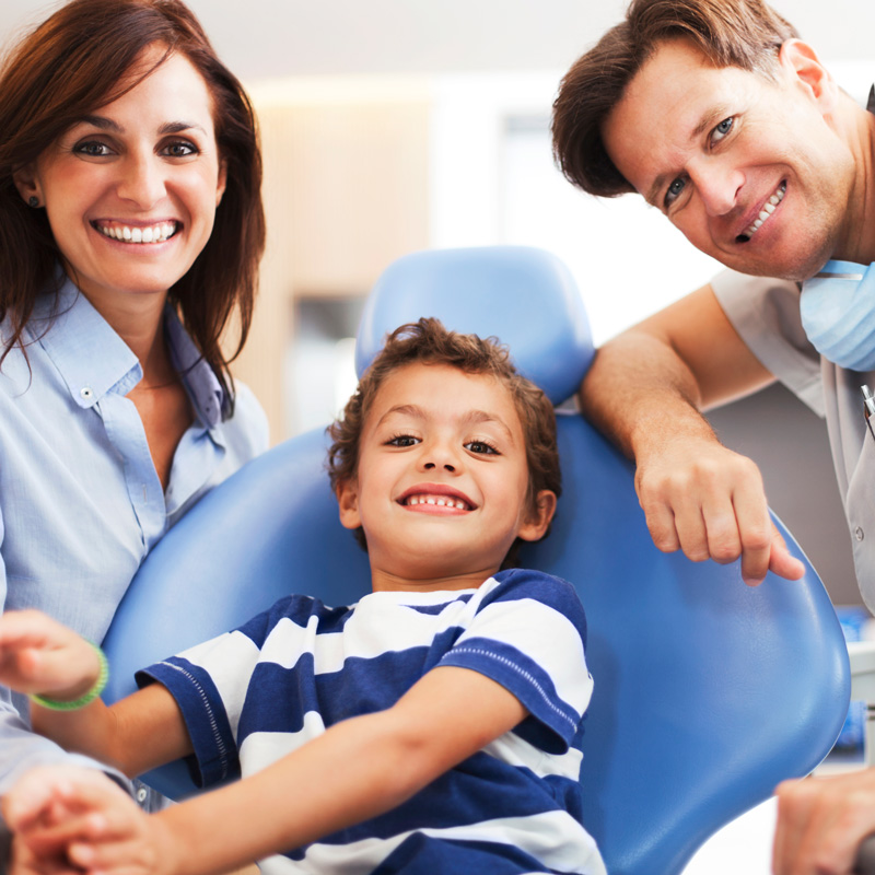 kid smiling in dental chair with dentist on either side